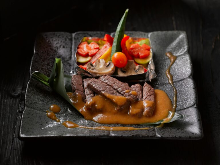 Elegant beef dish with vegetables and sauce on a dark plate, a culinary art piece.