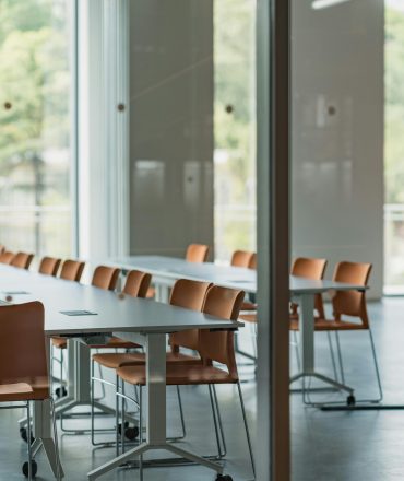 Spacious office interior featuring modern tables and orange chairs with large windows.