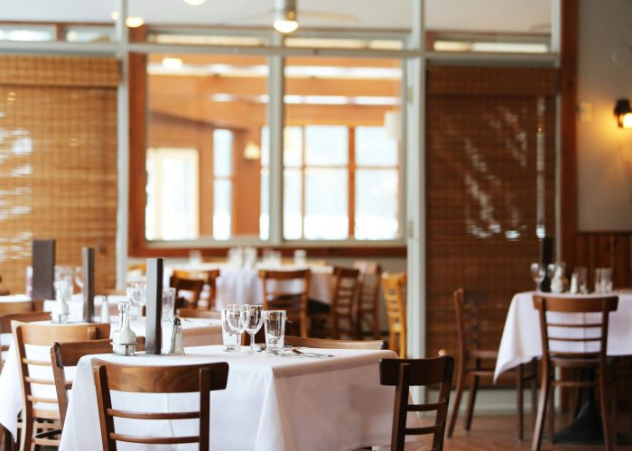 A serene restaurant interior with wooden chairs and tables set with glasses, ready for dining.